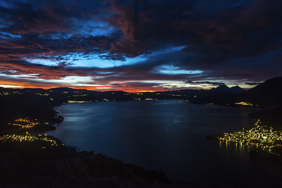 El lago en calma de noche con las luces de San Pedro La Laguna y la montaña.