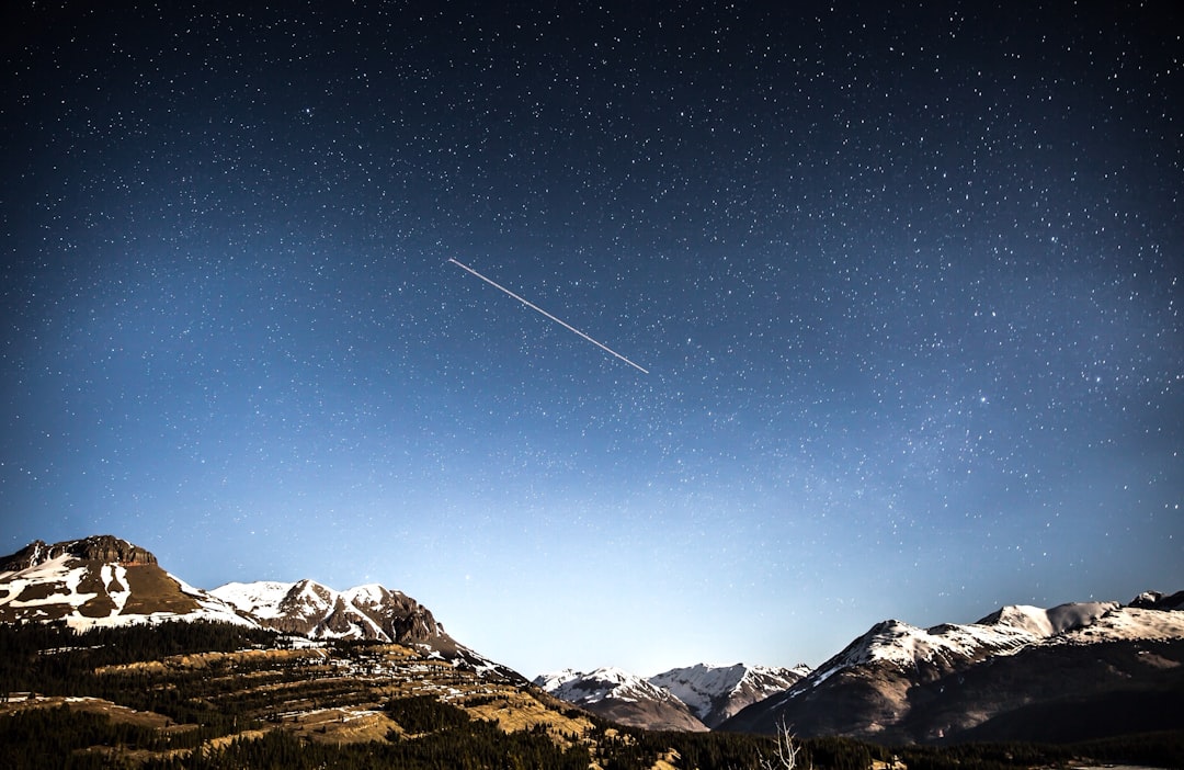 photo of shooting star over snow covered mountains