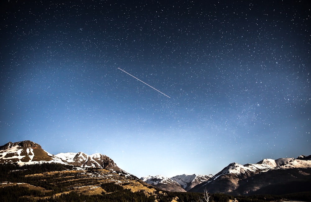 photo of shooting star over snow covered mountains