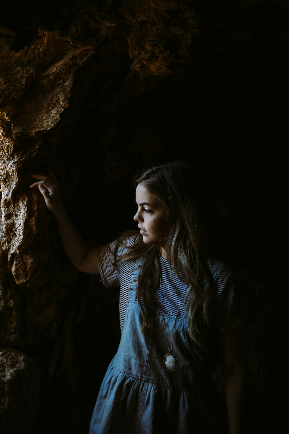 Mädchen trägt blau-weißes Kleid und hält sich an braunen Felsen fest