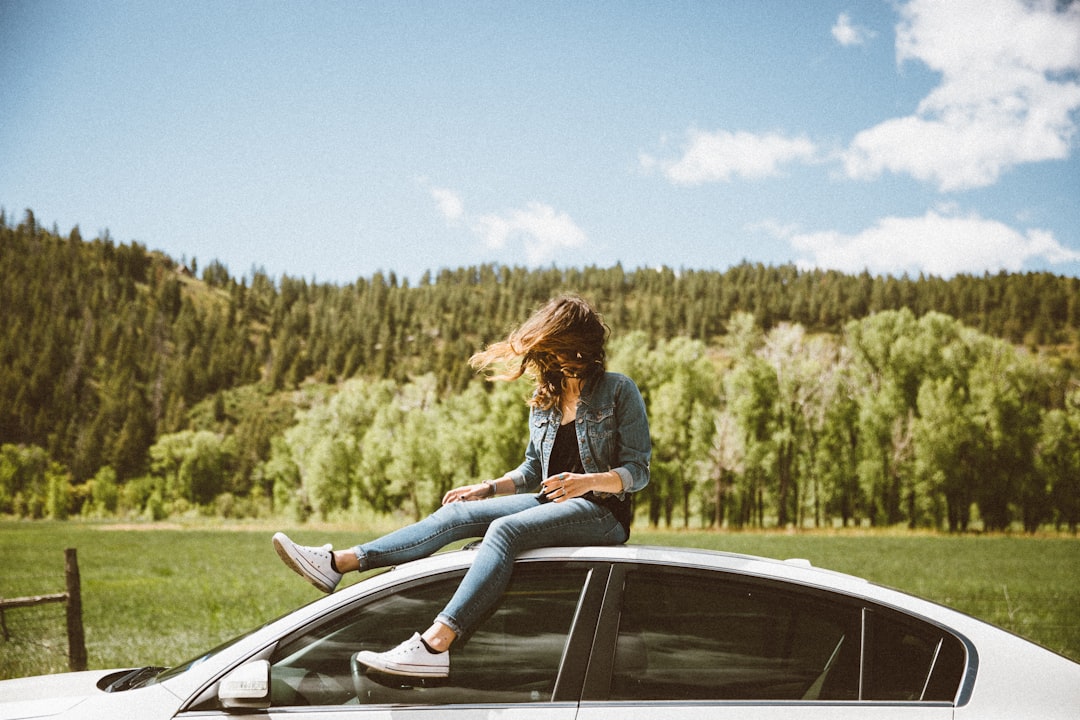 woman sitting on roof of white sedan