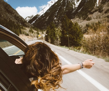 woman riding on vehicle putting her head and right arm outside the window while travelling the road