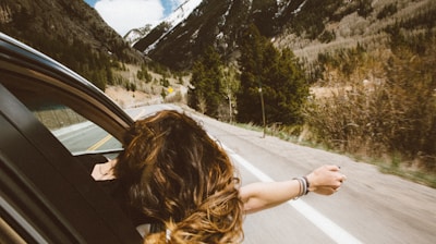 woman riding on vehicle putting her head and right arm outside the window while travelling the road