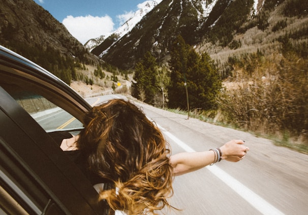 woman riding on vehicle putting her head and right arm outside the window while travelling the road