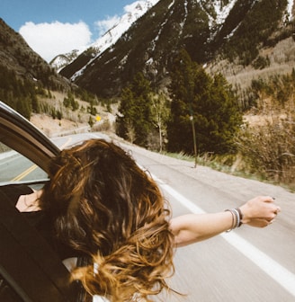 woman riding on vehicle putting her head and right arm outside the window while travelling the road