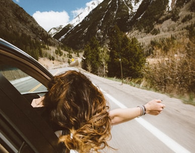 woman riding on vehicle putting her head and right arm outside the window while travelling the road