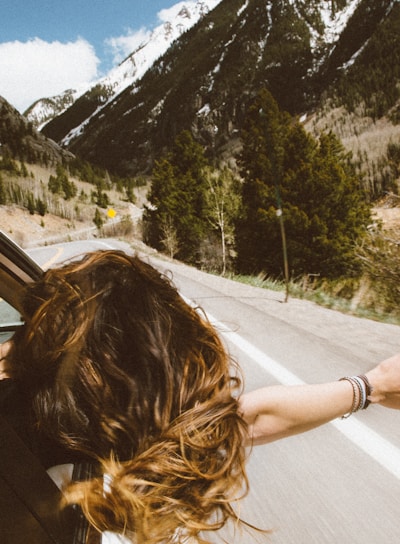 woman riding on vehicle putting her head and right arm outside the window while travelling the road