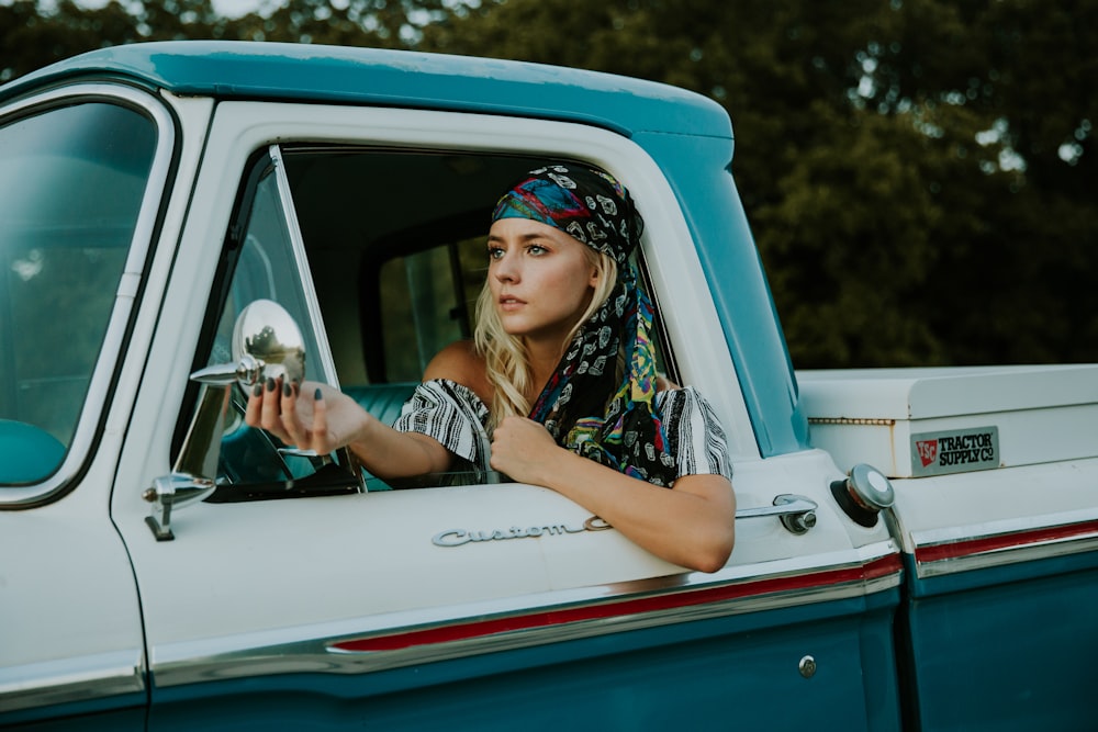 Photographie de femme tenant un rétroviseur latéral dans une camionnette 2 portes blanche et verte