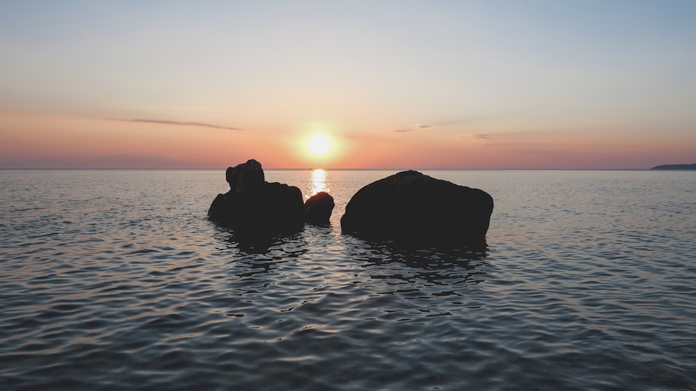 silhouette of rocks on body of water during golden hour