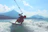 A smiling young woman holding a wakeboard by the lake with mountains in the background.