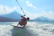 A smiling young woman holding a wakeboard by the lake with mountains in the background.