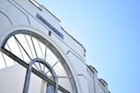 An architectural detail of a white building with an arched window and metallic framing. The word 'INSULINDE' is displayed prominently on a sign above the arch. The sky is clear and blue, adding to the clean and modern aesthetic.