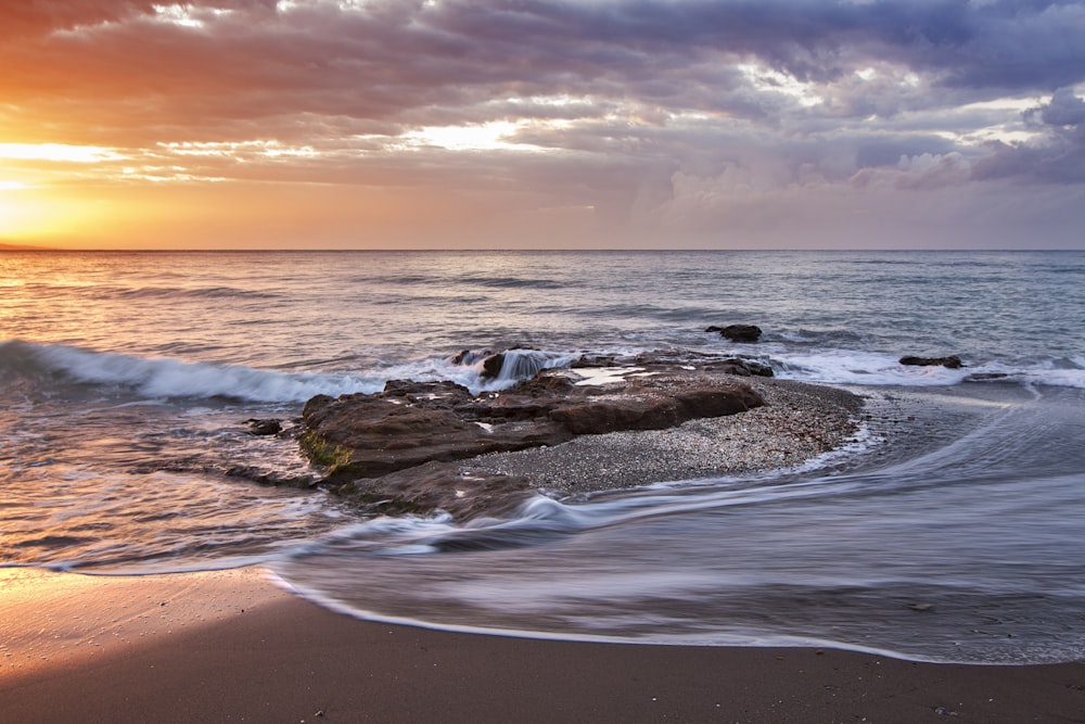 brown stone near seashore during sunset