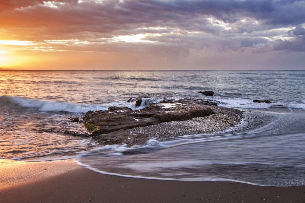 Pedra marrom perto da costa durante o pôr do sol