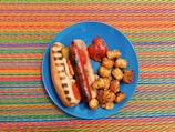 A colorful hot dog topped with mustard, ketchup, and chopped onions on a plate.