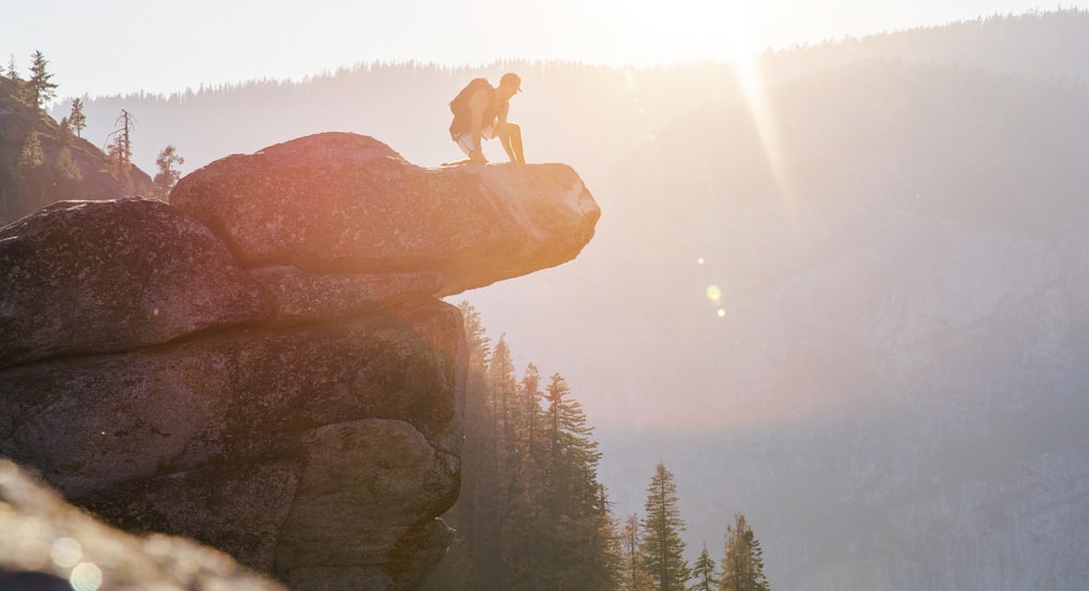 A person kneeling on the ledge of a rock with the sunset in the background at Glacier Point