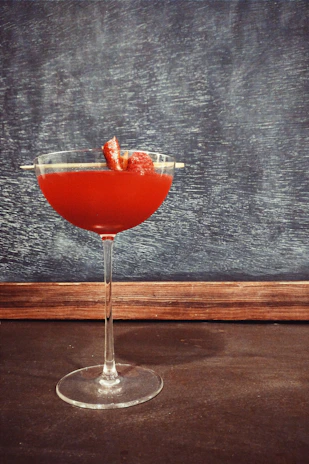 A vibrant red cocktail with a sugared rim and a fresh strawberry perched on the edge.