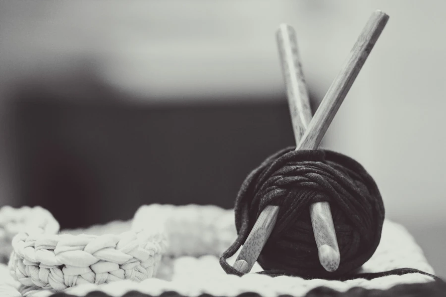 A ball of dark yarn with needles resting on a chunky hand-knitted blanket