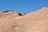 Smooth sandstone formations gently rise against a clear blue sky, showcasing layered rock formations with subtle shades of peach and tan. The terrain appears barren and expansive, with undulating curves that suggest erosion over time.