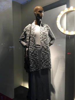 Flowing midi dress in muted grey tones displayed on a mannequin with natural light highlighting fabric texture.