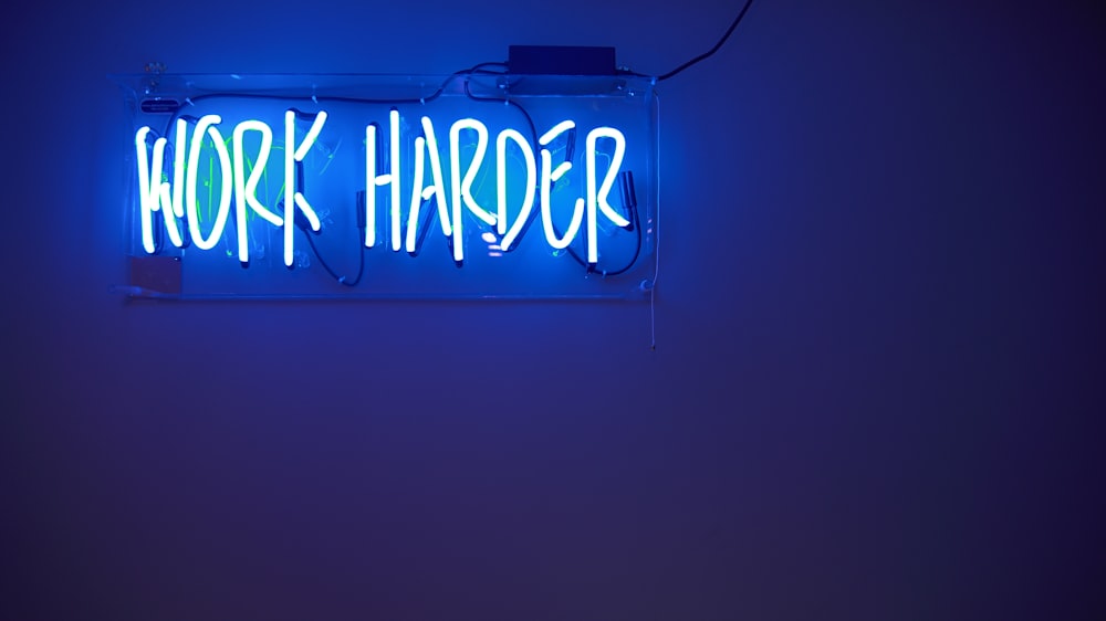 A bright blue neon on a wall reads â€œWork harderâ€