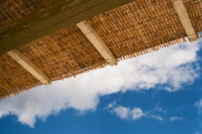 A bamboo roof or canopy stretches across the top of the frame against a backdrop of a clear blue sky with scattered white clouds.