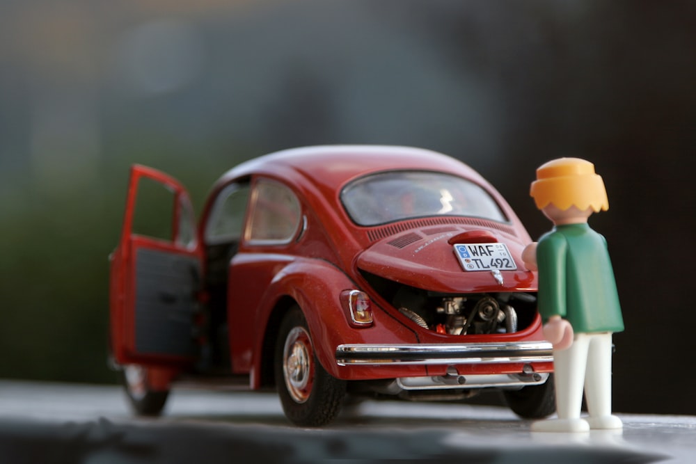 cabelo laranja Lego brinquedo olhando para o carro besouro vermelho
