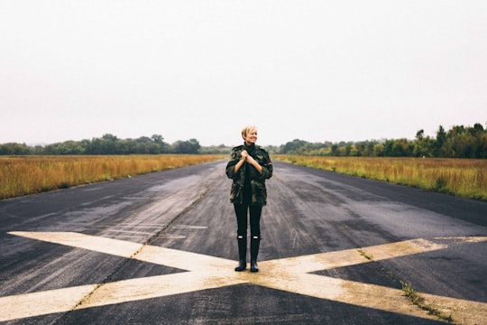 woman standing on black asphalt between green grass under clear blue sky during daytime in Cornelia Fort Airport United States