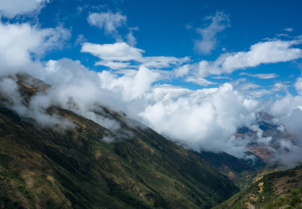 view of mountain covered with green grass and white clouds during daytime