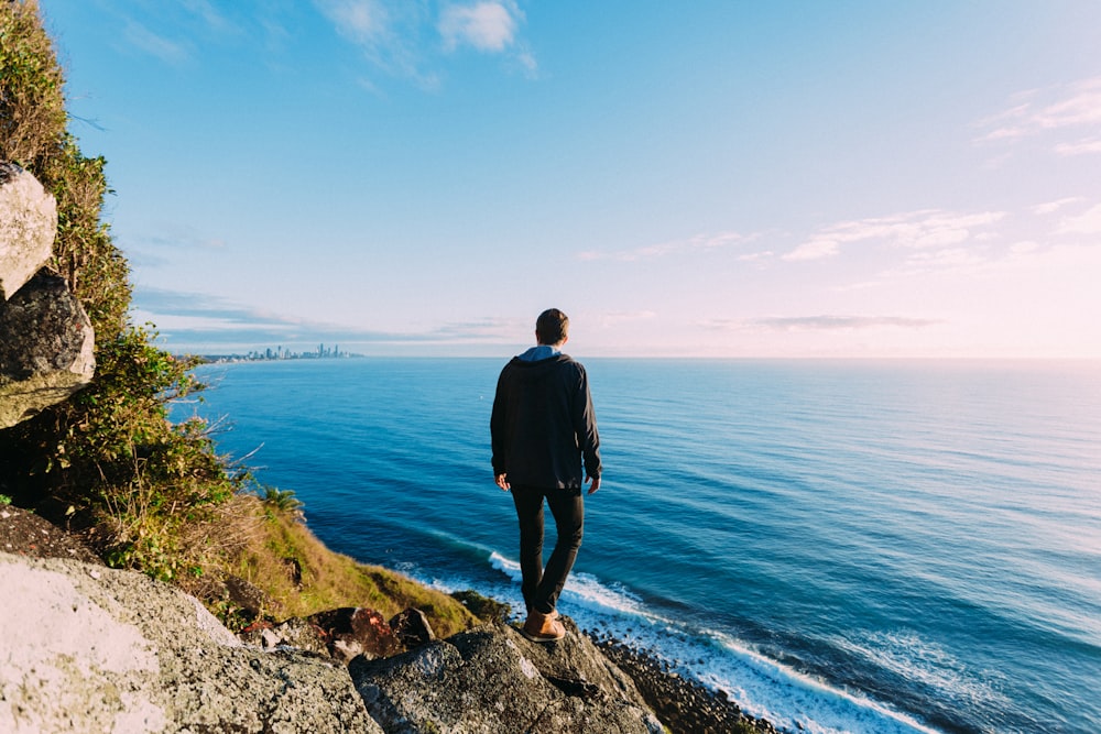 man standing on rock cliff near sea