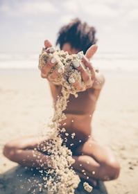 Hands holding a sand can with a beach and waves in the blurred background.