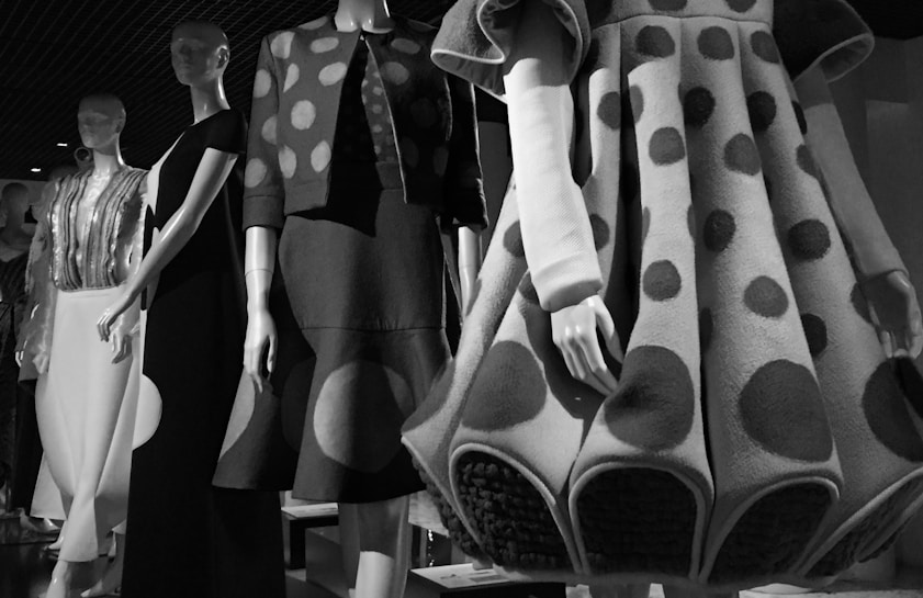 A series of mannequins display fashion clothing with various styles, including polka dot patterns and textured fabrics. The scene is captured in black and white, highlighting the intricate details of the garments.