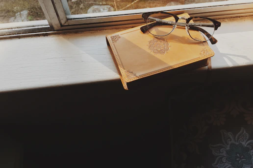 Calm workspace with a journal, pen, and eyeglasses on a wooden table, soft morning light.