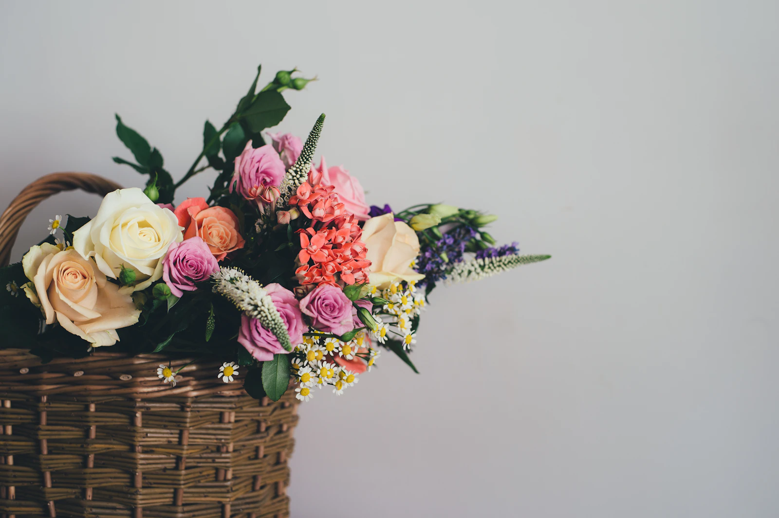 Assorted flowers arranged in a brown wicker hamper basket