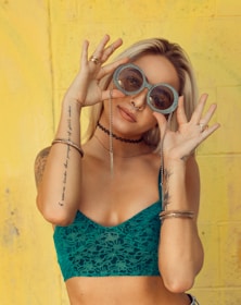 woman in blue bralette holding sunglasses putting on her eyes
