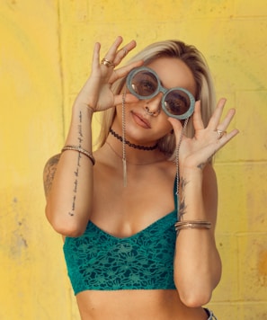 woman in blue bralette holding sunglasses putting on her eyes