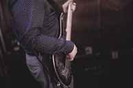 A person wearing a dark, polka-dotted shirt is playing an electric guitar. The focus is on the torso and arm, highlighting the guitar strings and picking technique.