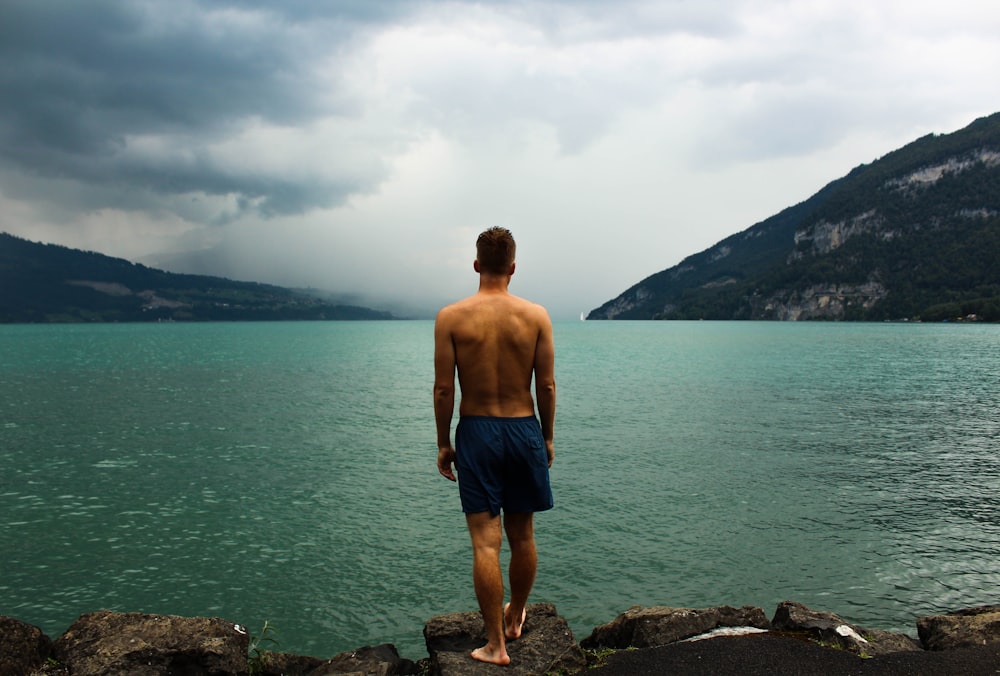 hombre con pantalones cortos negros parado frente a un cuerpo de agua