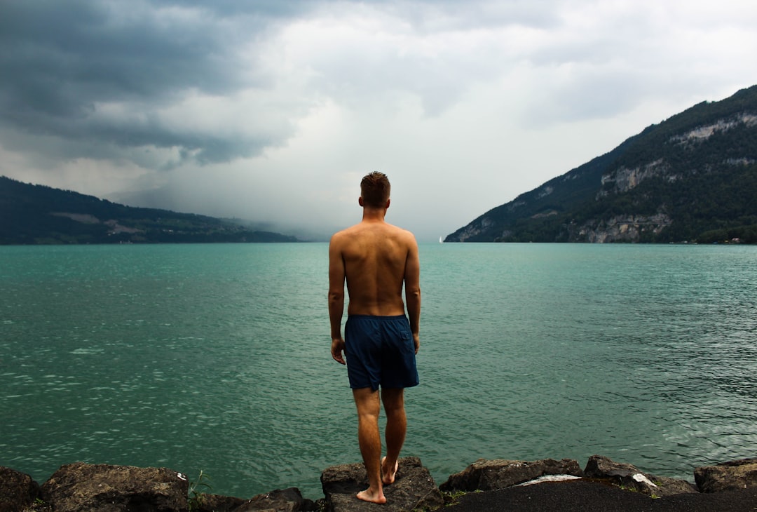 man wearing black shorts standing in front of body of water, Swimming at the Lake