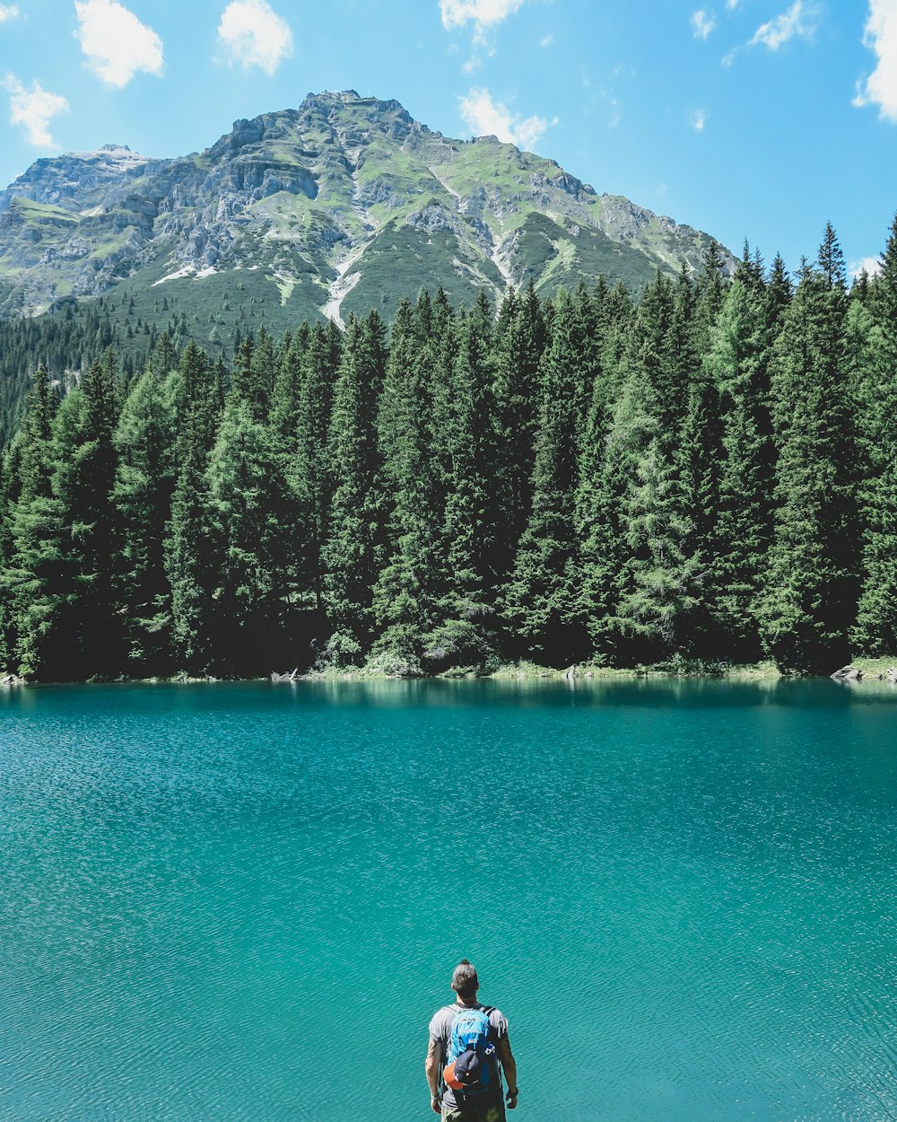 man looking through on lake with pine trees under blue sky