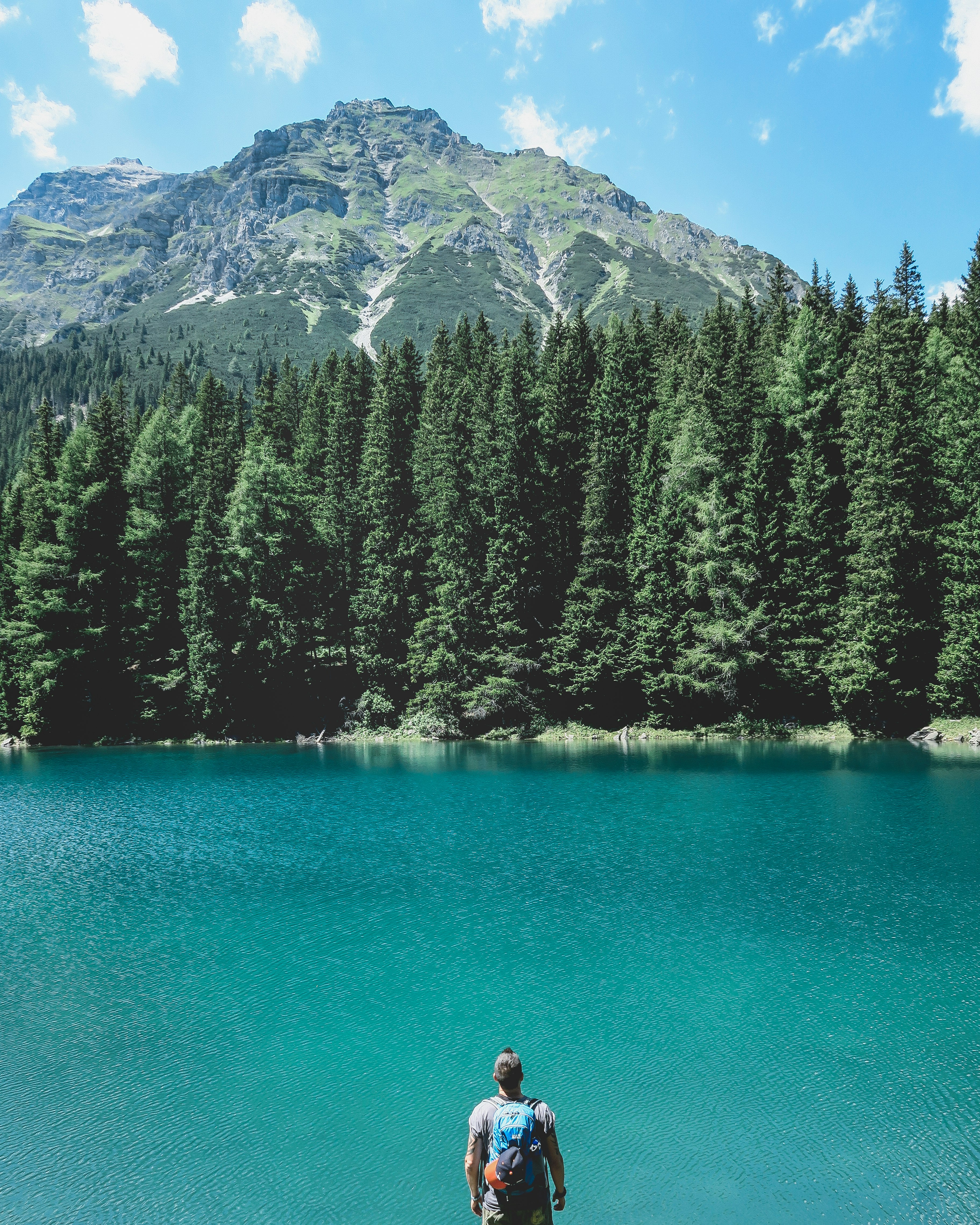 man looking through on lake with pine trees under blue sky