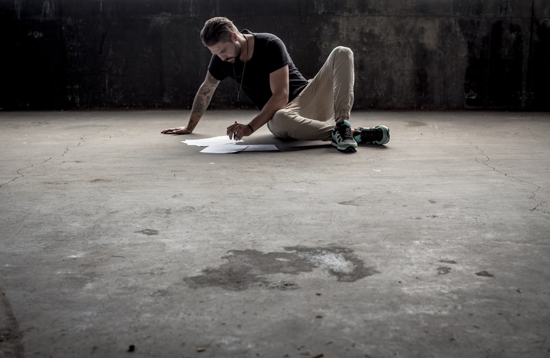 A man with a pen looking at sheets of paper while seated on a concrete industrial floor