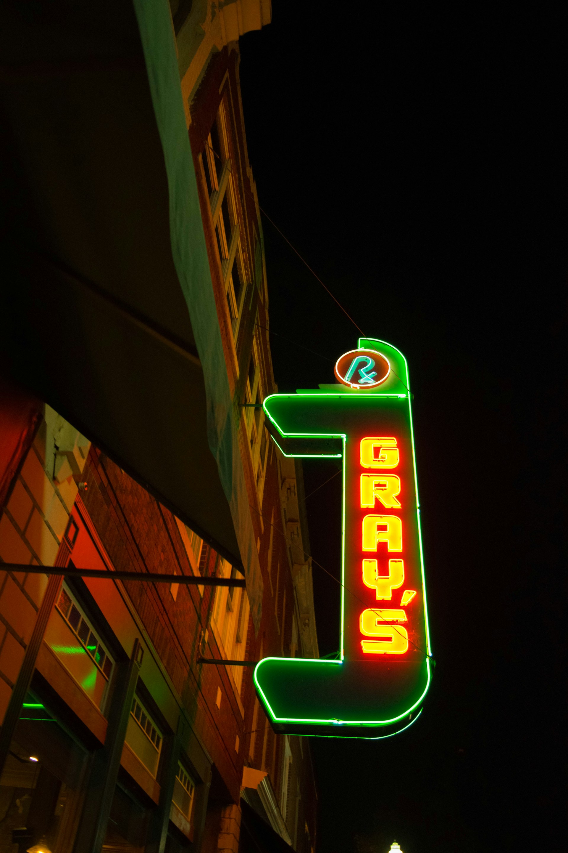 A neon sign at night displaying the word 'GRAY'S' in bright red letters outlined in green. The sign is mounted on a building with visible windows, and the scene is framed against a dark sky.
