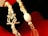 A close-up view of a decorative bracelet featuring a floral-designed clasp. The bracelet is composed of various beads including pearls, crystal-like beads, and metallic elements, all arranged on a bright red and black background.