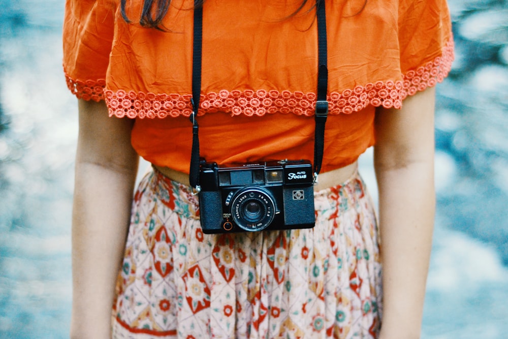 オレンジ色と色とりどりのドレスを着て、首に黒いブリッジカメラをつけた女性