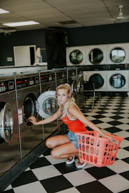 woman kneeling in front of front-load clothes washer inside laundry shop