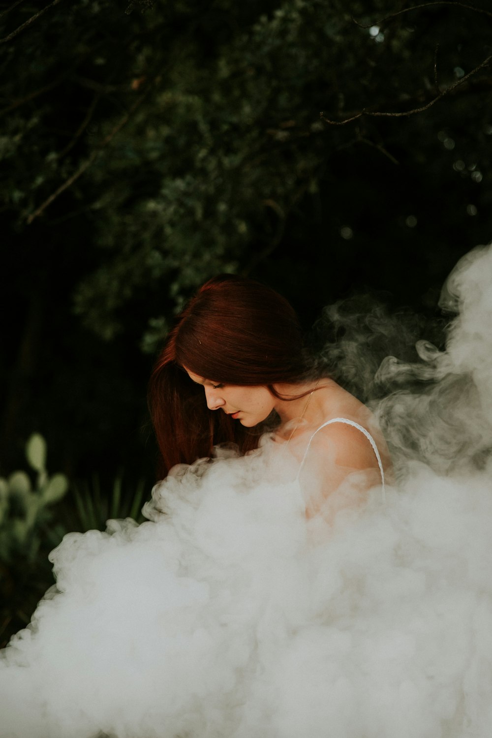 donna in camicia senza maniche bianca con spalline sottili in piedi vicino agli alberi ha coperto il suo corpo di fumo