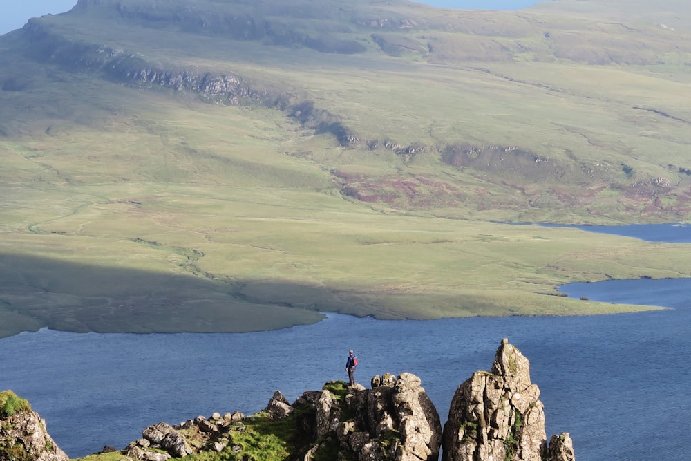 man standing at top of rock formation beside sea near mountains