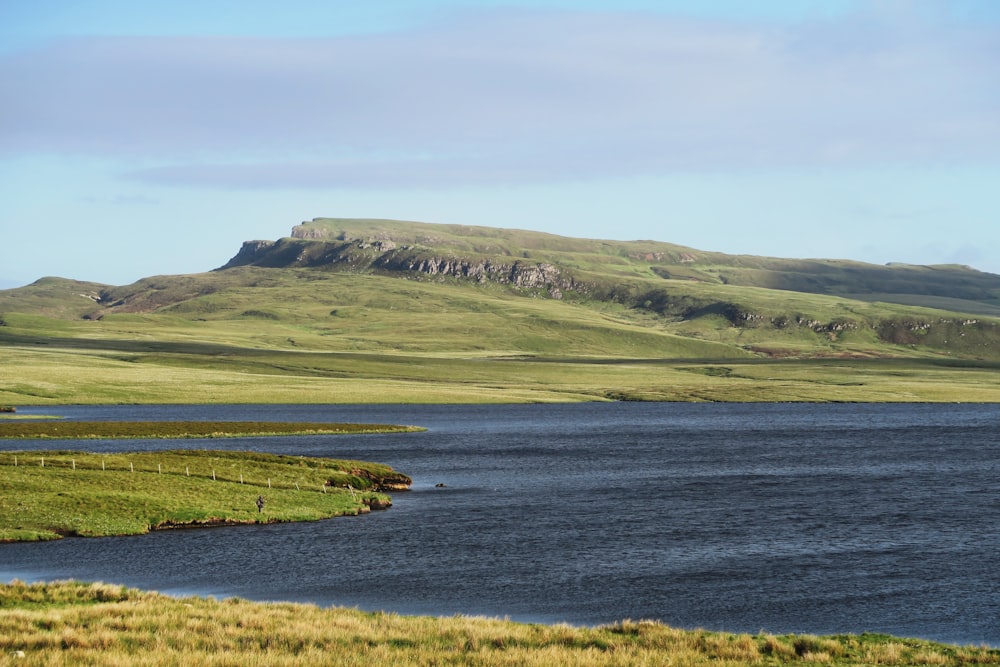 body of water surrounded by green mountain under clear blue sky during daytime