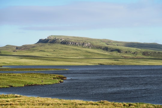 body of water surrounded by green mountain under clear blue sky during daytime in Portree United Kingdom